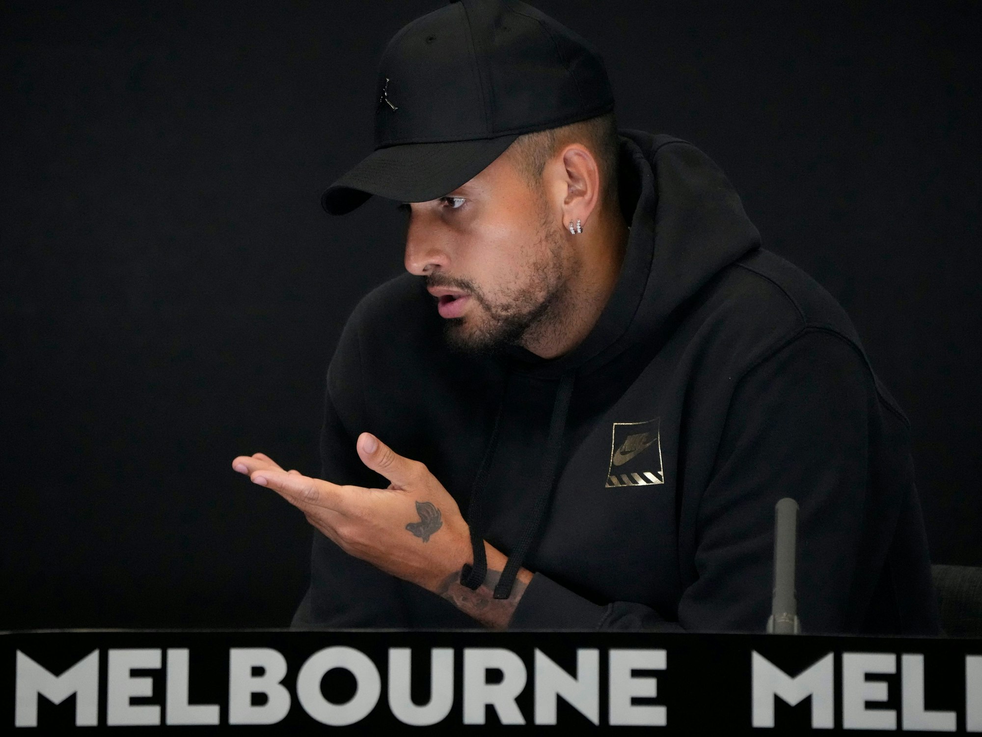 Nick Kyrgios spricht mit Baseball-Kappe bei einer pressekonferenz.