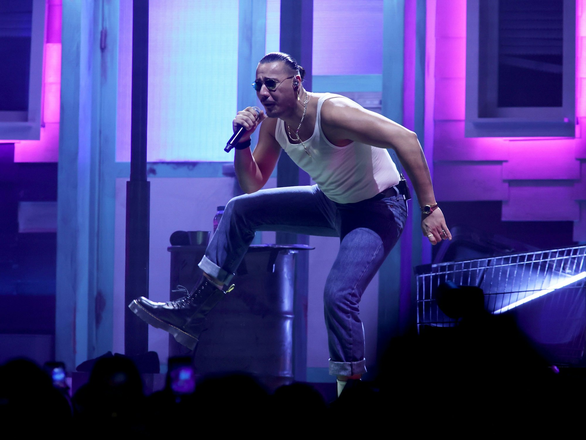 Apache 207 steht in Köln auf der Bühne und hebt sein Bein.