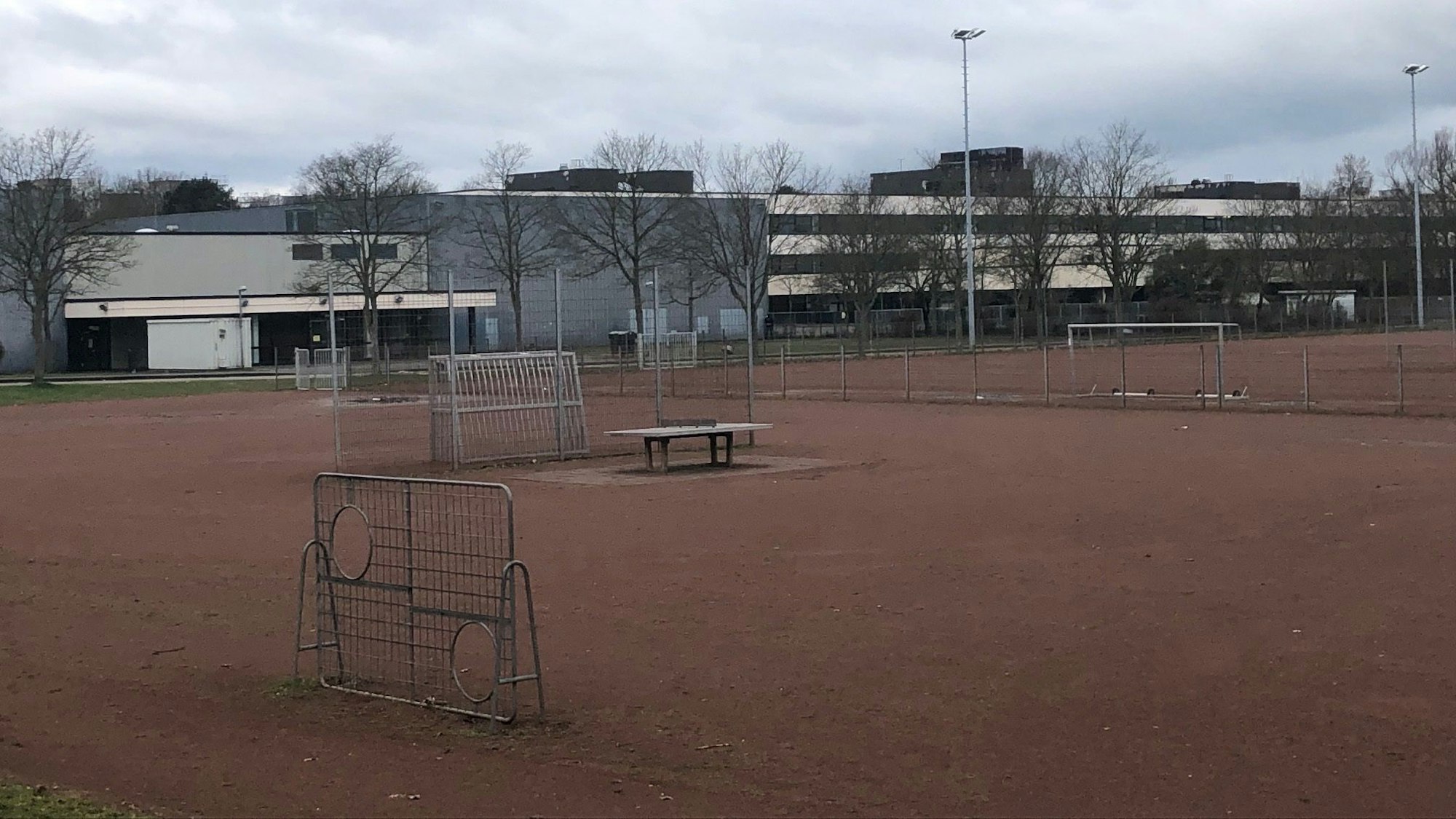 Blick auf die Heinrich-Böll-Gesamtschule in Chorweiler. Im Vordergrund ist ein Ascheplatz zu sehen.