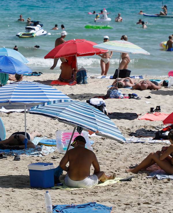 Menschen liegen am Strand von Cala Major, in der Nähe von Palma auf Mallorca, oder halten sich im Wasser auf.