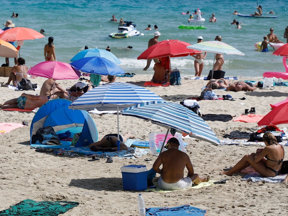 Symbolfoto: Menschen liegen am Strand von Cala Major, in der Nähe von Palma auf Mallorca, oder halten sich im Wasser auf.