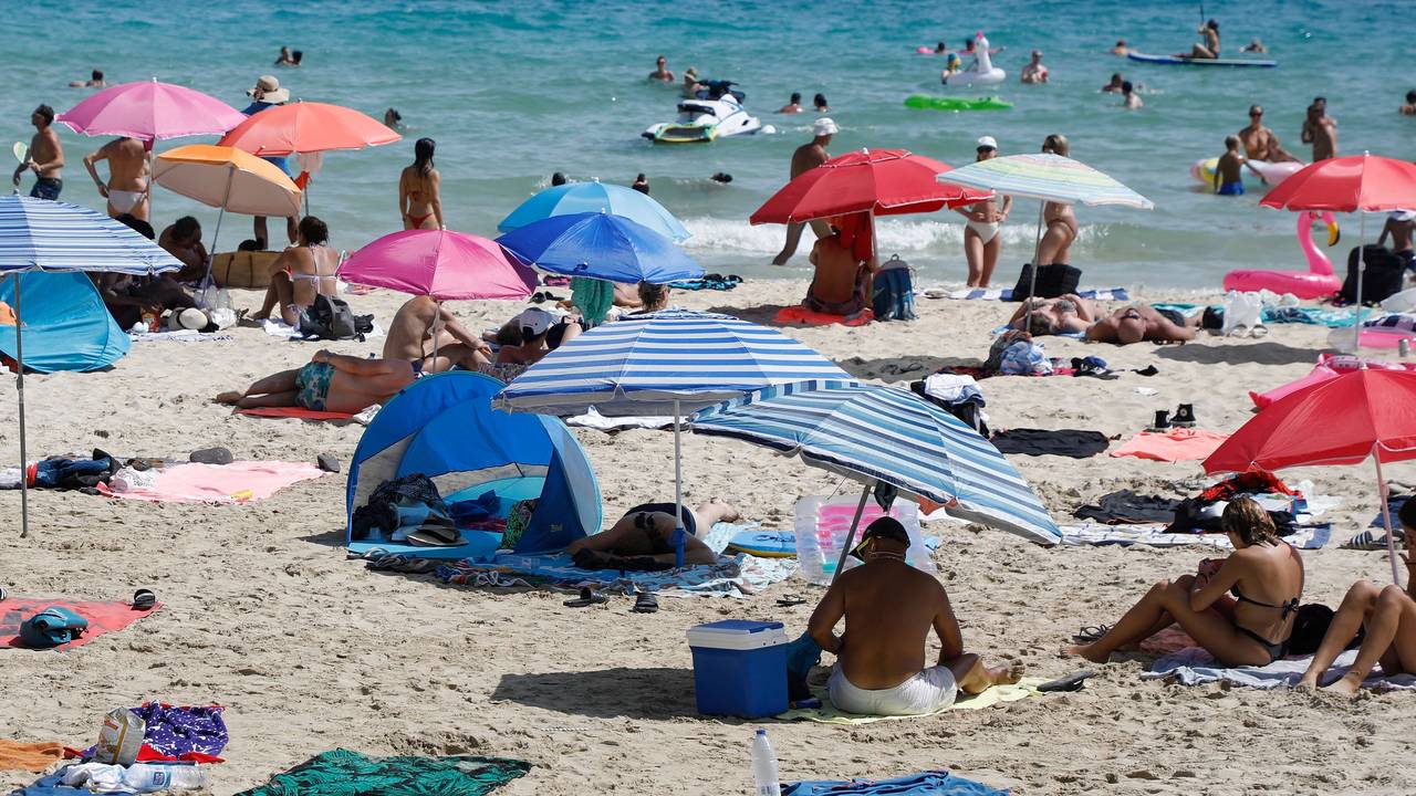 Menschen liegen am Strand von Cala Major, in der Nähe von Palma auf Mallorca, oder halten sich im Wasser auf.