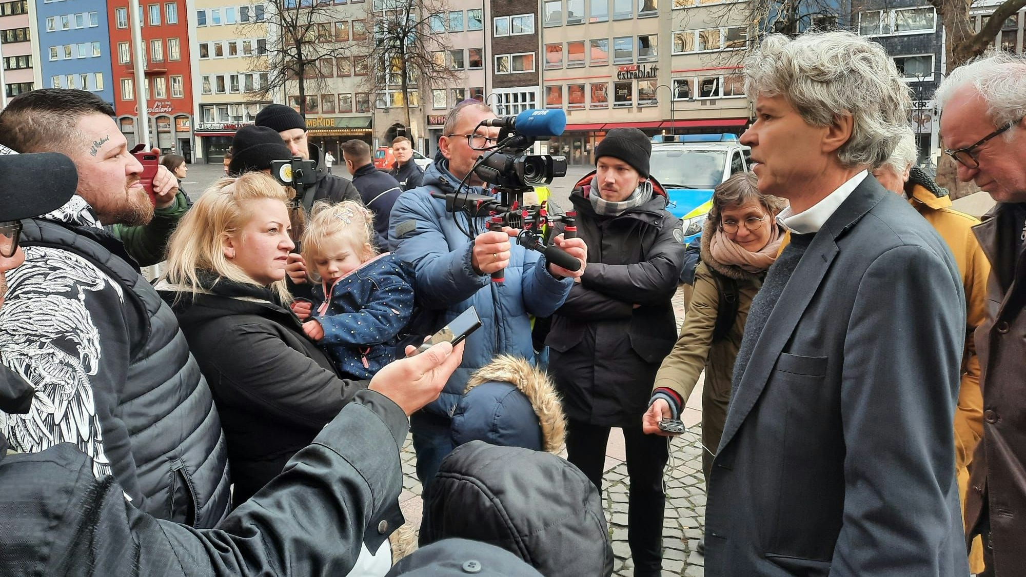Menschen stehen um Sozialdezernent Harald Rau herum, ein Kameramann filmt ihn.