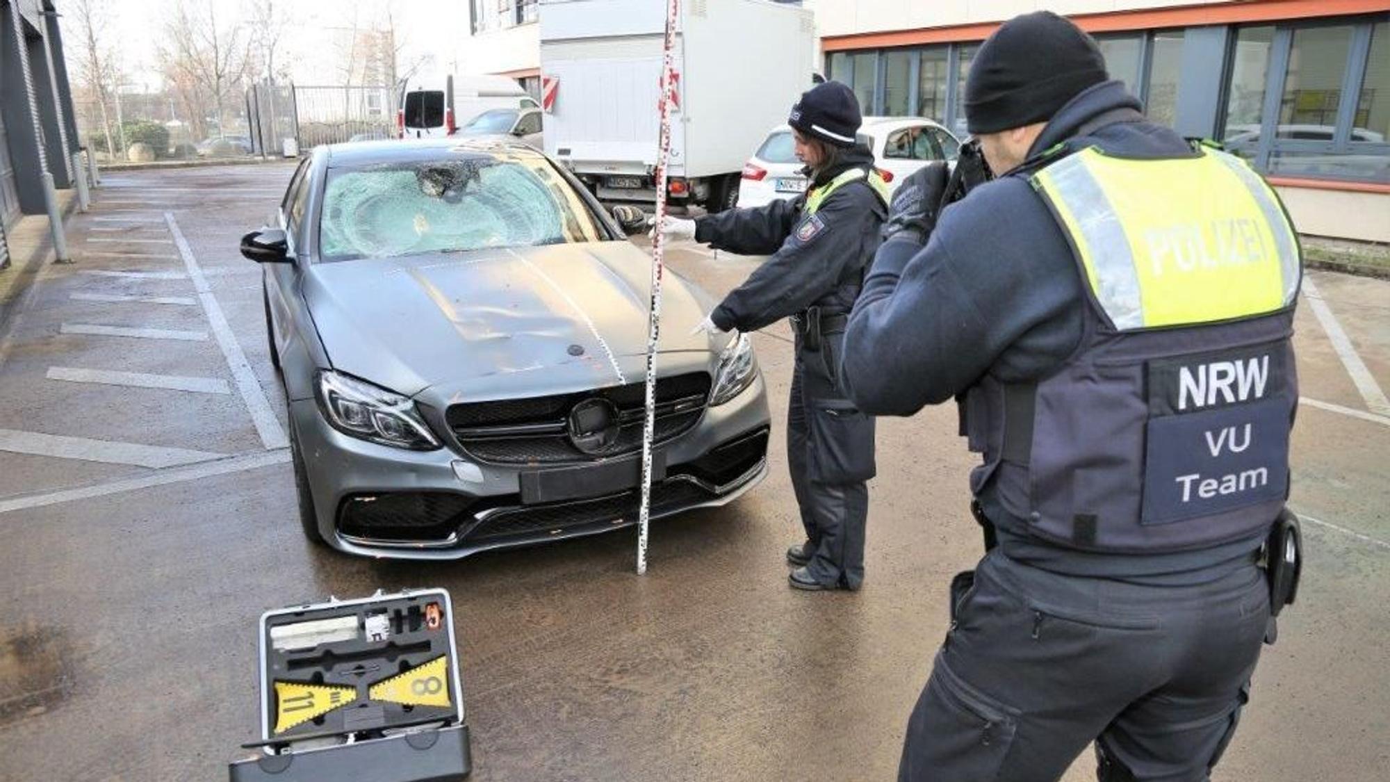Eine Polizistin hält einen Maßstab an den sichergestellten Mercedes, ihr Kollege macht Fotos.
