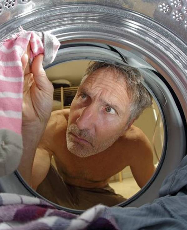 Mann schaut in Waschmaschine nach verlorenen Socken