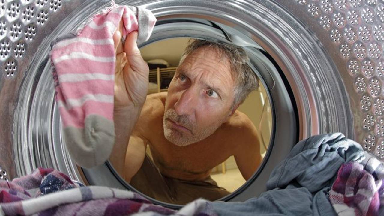 Mann schaut in Waschmaschine nach verlorenen Socken