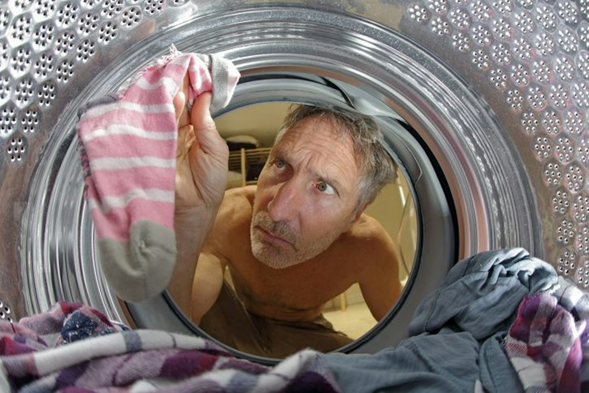 Mann schaut in Waschmaschine nach verlorenen Socken