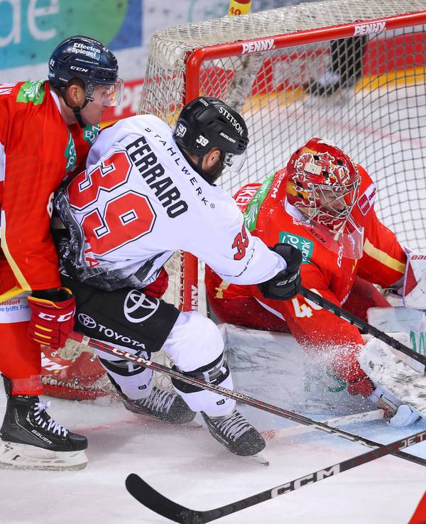 Landon Ferraro von Kölner Haie schießt den Puck auf das Tor von Düsseldorfs Henrik Haukeland und wird dabei von Stephen MacAulay in Bedrängnis gebracht.