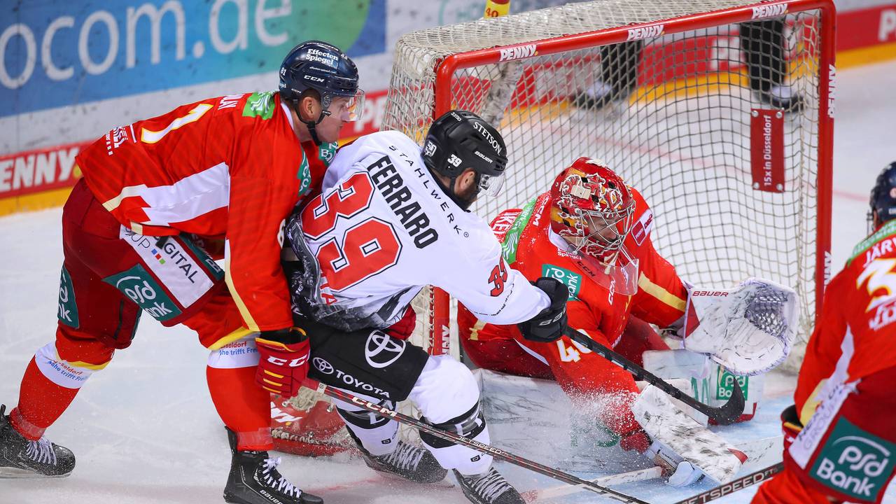 Landon Ferraro von Kölner Haie schießt den Puck auf das Tor von Düsseldorfs Henrik Haukeland und wird dabei von Stephen MacAulay in Bedrängnis gebracht.