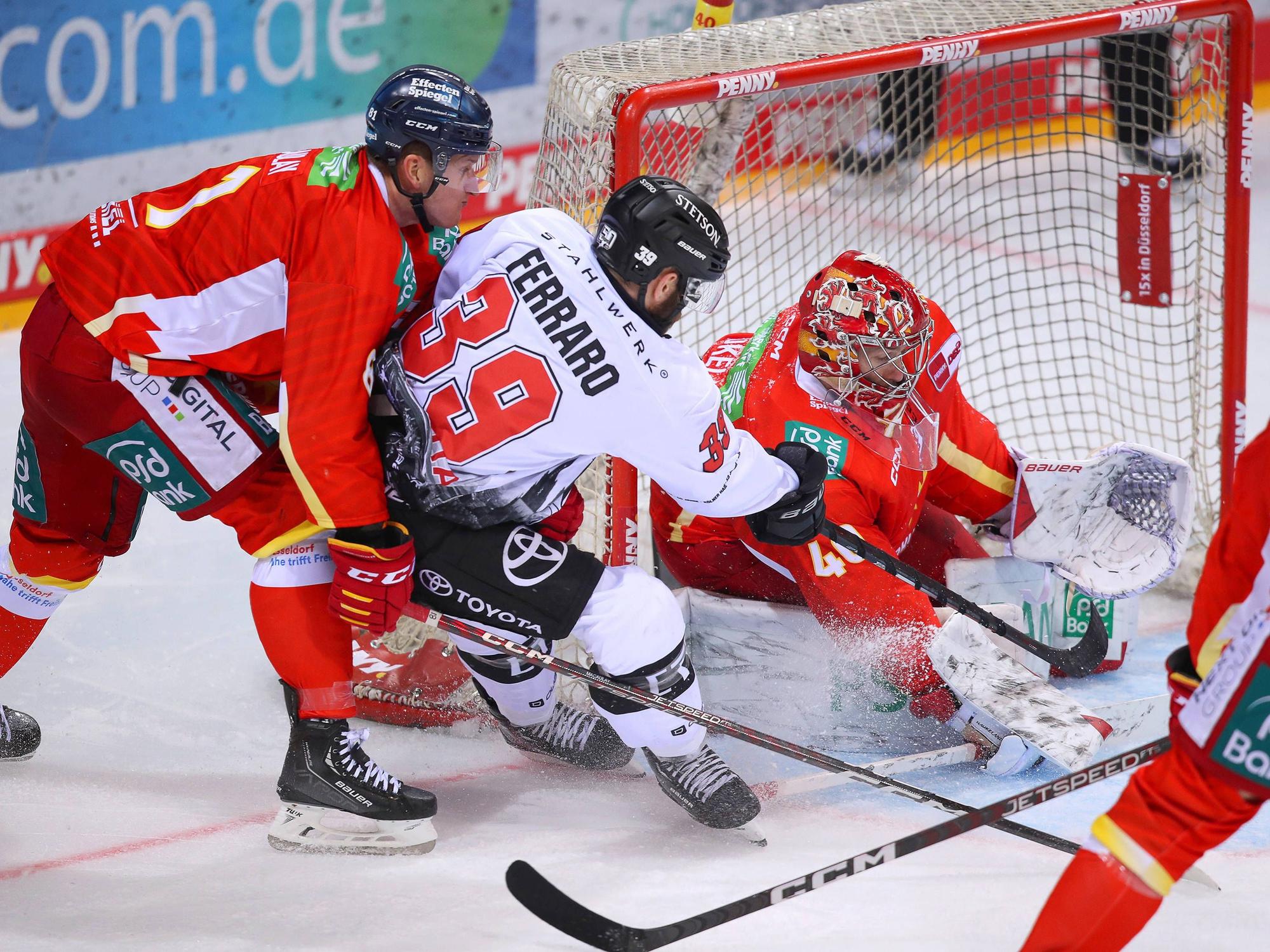 Landon Ferraro von Kölner Haie schießt den Puck auf das Tor von Düsseldorfs Henrik Haukeland und wird dabei von Stephen MacAulay in Bedrängnis gebracht.