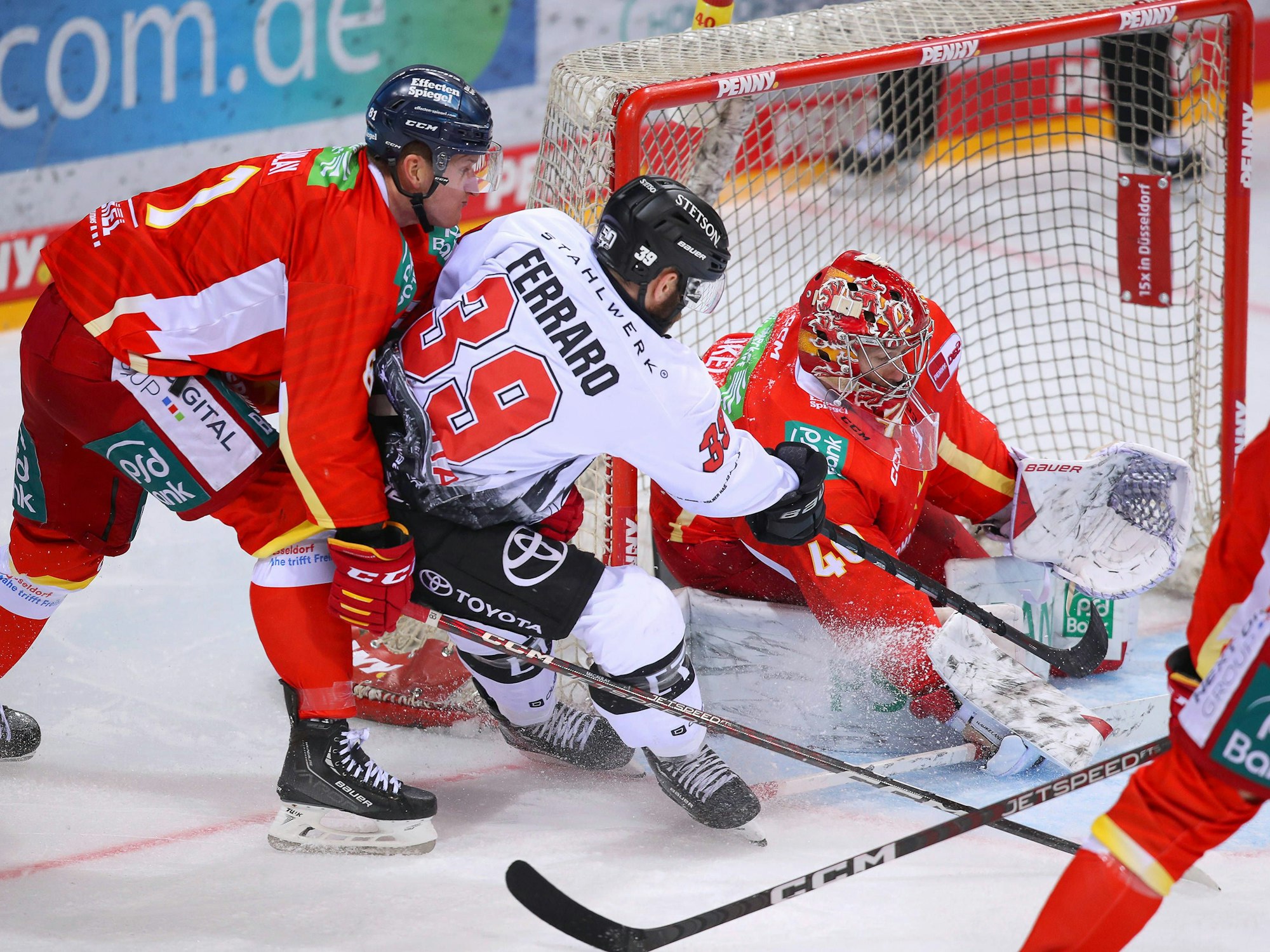 Landon Ferraro von Kölner Haie schießt den Puck auf das Tor von Düsseldorfs Henrik Haukeland und wird dabei von Stephen MacAulay in Bedrängnis gebracht.