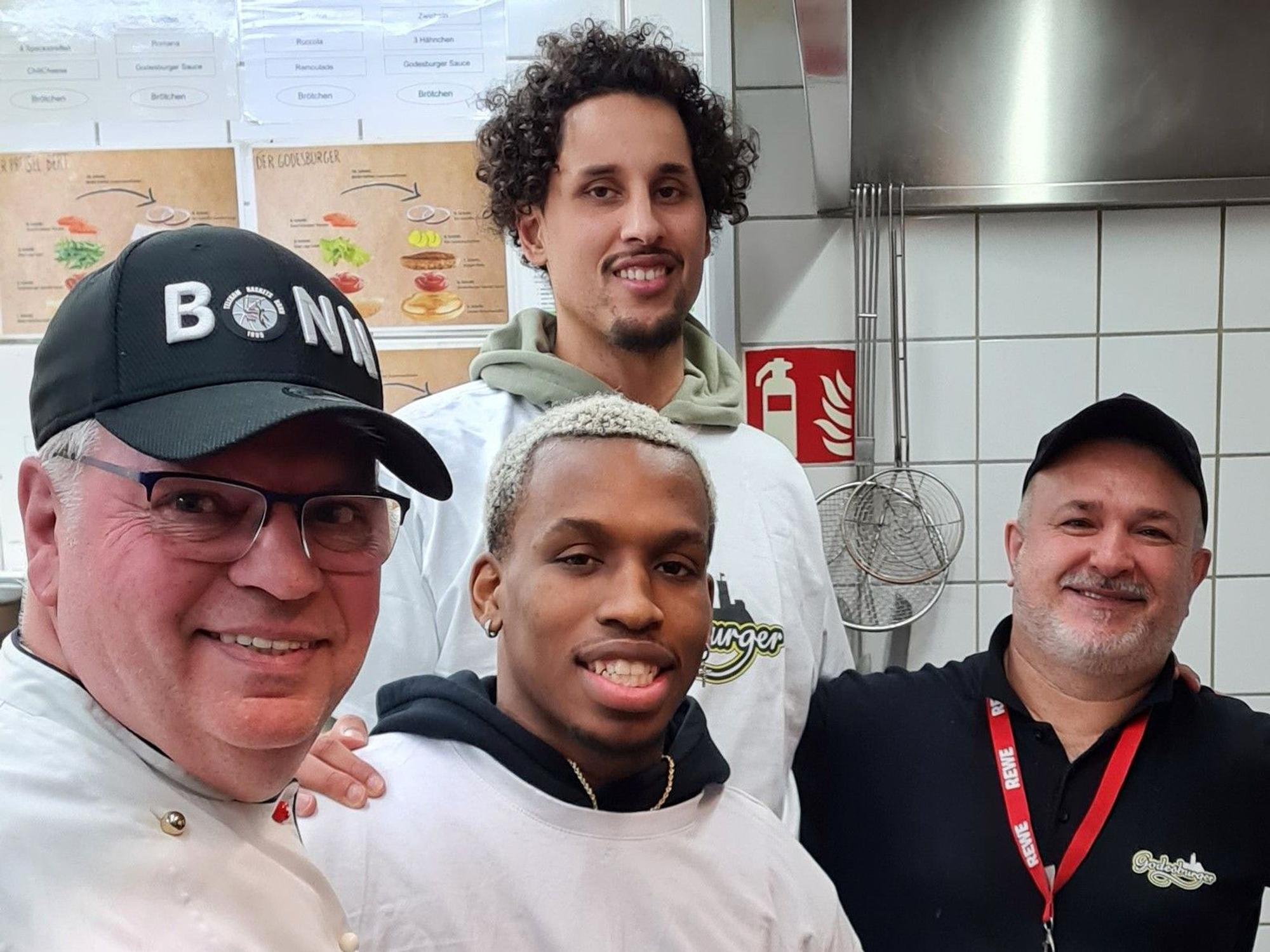 Restaurantleiter Bruno Straub, Point Guard TJ Shorts II, Center Michael Kessens und Beikoch Davut Dere-Knapp stehen in der Küche des „Godesburgers“.
