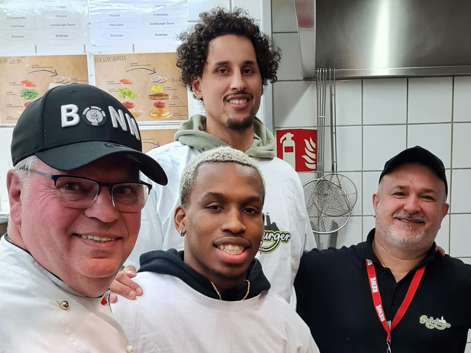 Restaurantleiter Bruno Straub, Point Guard TJ Shorts II, Center Michael Kessens und Beikoch Davut Dere-Knapp stehen in der Küche des „Godesburgers“.
