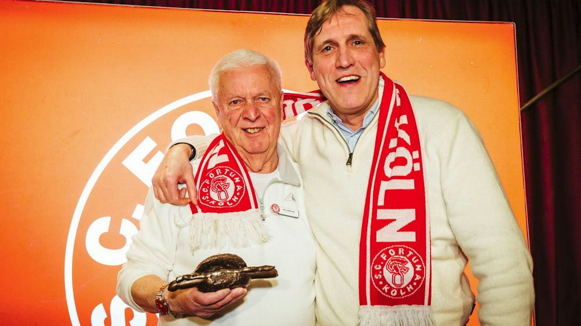 Fortuna-Urgestein Paul Sennelaub hält die „Bronzene Stadionwurst“ in der Hand, Künstler Cornel Wachter legt den Arm um ihn.