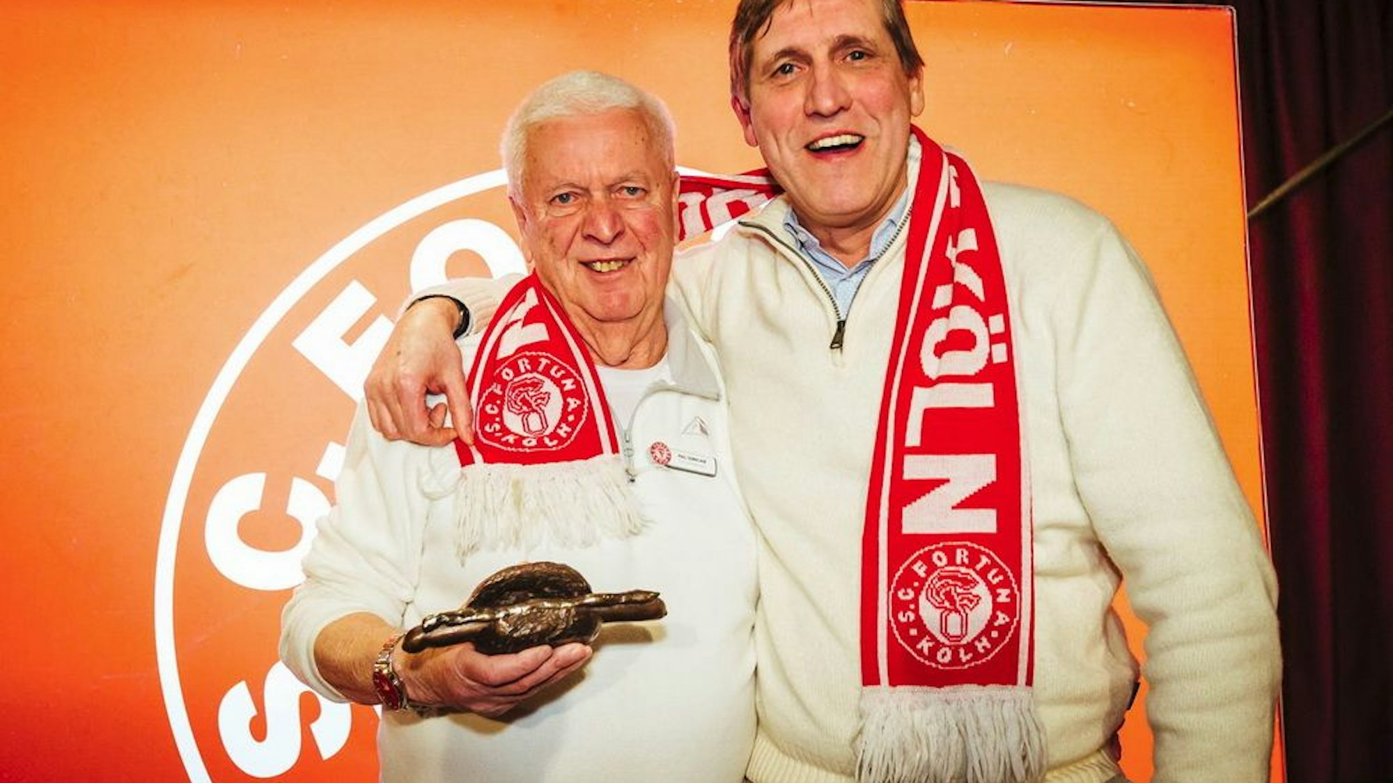 Fortuna-Urgestein Paul Sennelaub hält die "Bronzene Stadionwurst" in der Hand und wird von Künstler Cornel Wachter umarmt.