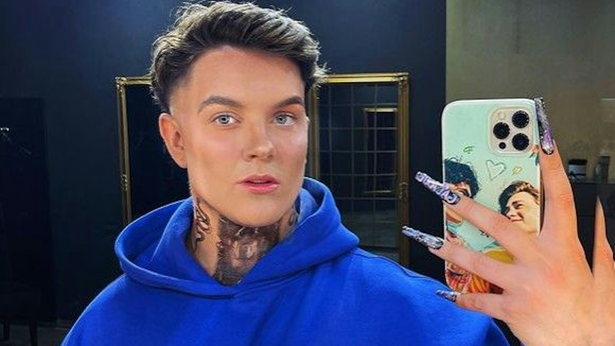 Influencer Twenty4Tim lächelt in einem blauen Pullover in die Handy-Kamera.