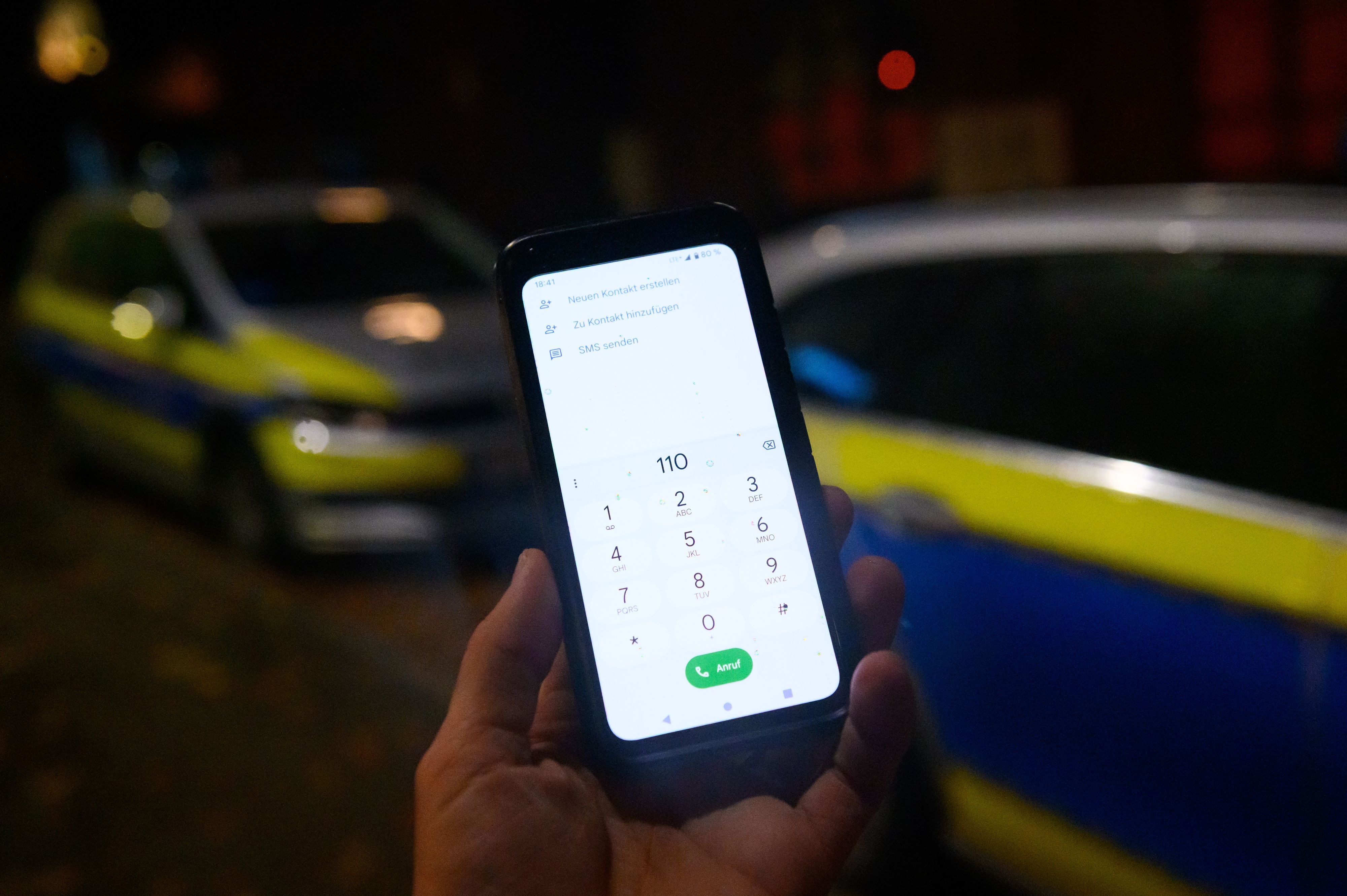 Die Notrufnummer „110“ ist auf einem Smartphone eingegeben, dass vor zwei Streifenwagen gehalten wird.