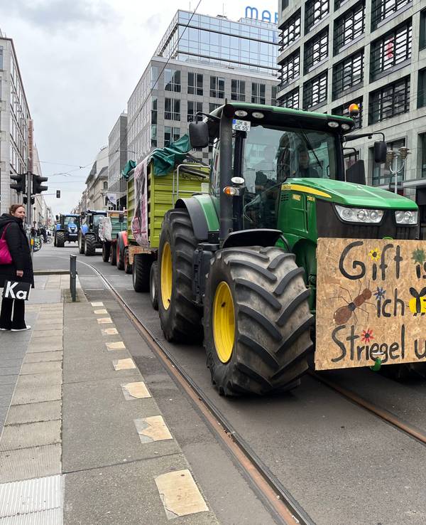 Ein Traktor mit einem Protestplakat fährt durch die noble Berliner Friedrichstraße.
