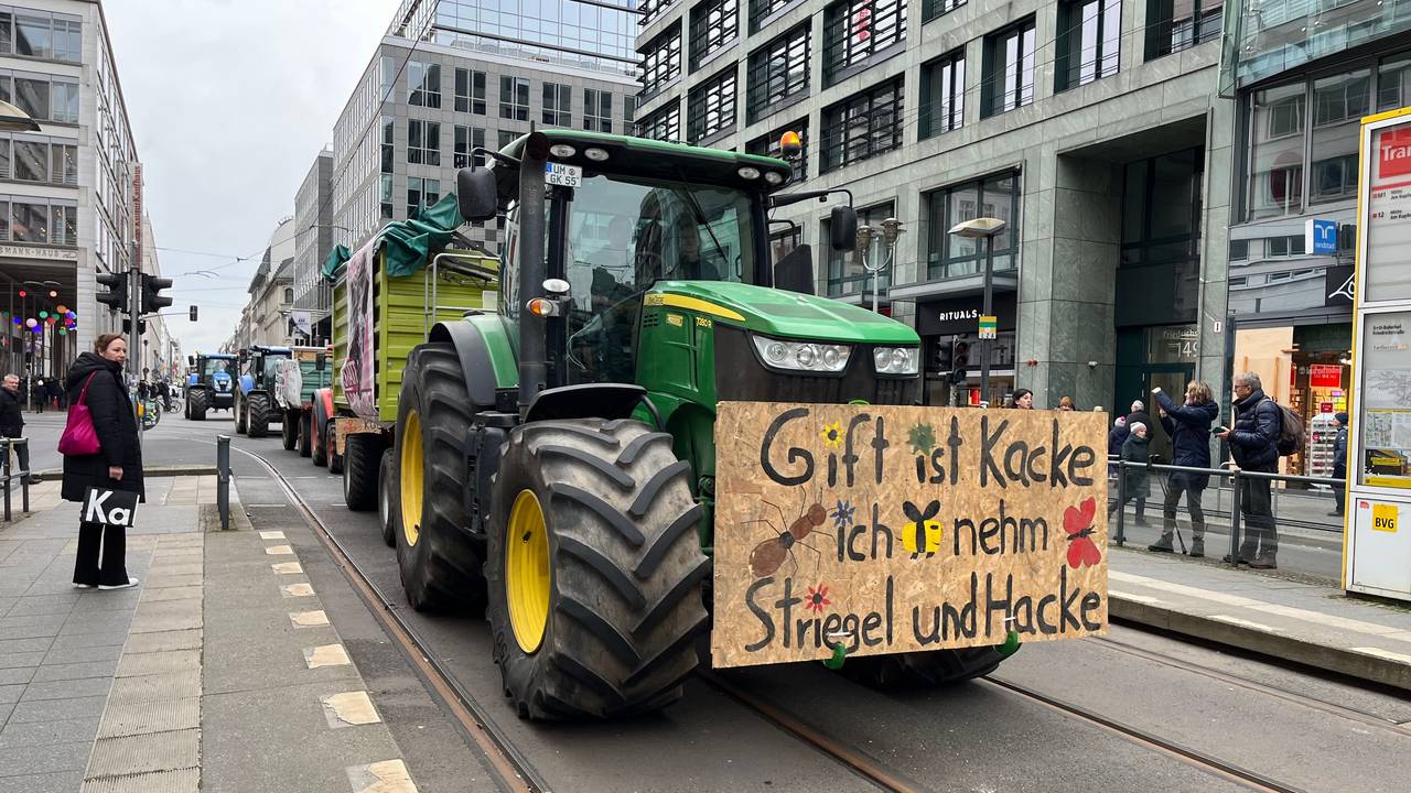 Ein Traktor mit einem Protestplakat fährt durch die noble Berliner Friedrichstraße.