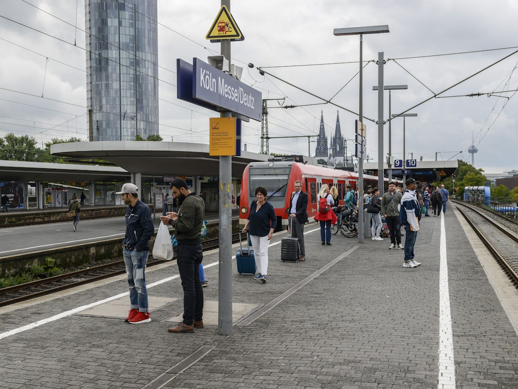 Menschen warten am Bahnsteig in Köln Messe/Deutz auf einen Zug.