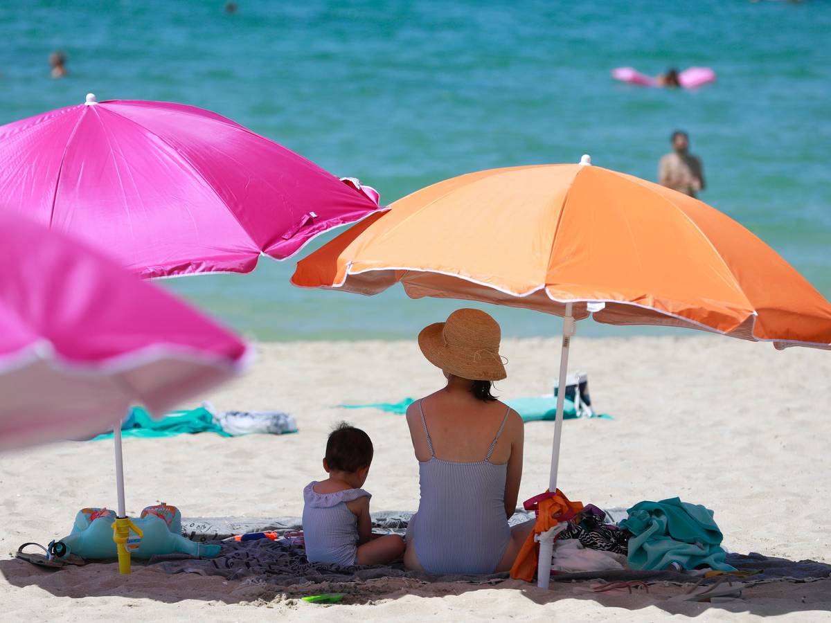 Eine Frau sitzt neben ihrem Kind unter einem Sonnenschirm an einem warmen Sommertag am Strand von Mallorca.