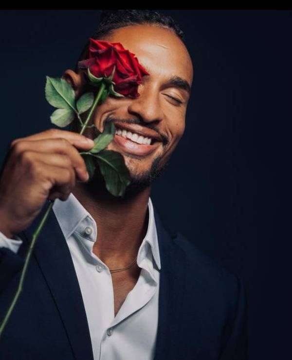 Er ist der neue „Bachelor“: David Jackson geht auf Liebessuche im TV. Er hält sich eine Rose vor sein Auge und trägt ein Anzug.