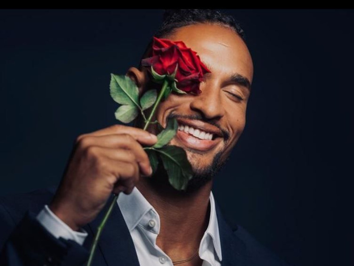 Er ist der neue „Bachelor“: David Jackson geht auf Liebessuche im TV. Er hält sich eine Rose vor sein Auge und trägt ein Anzug.