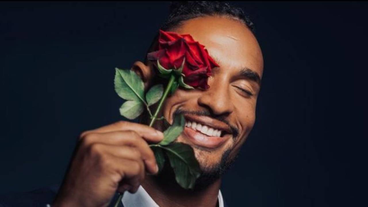 Er ist der neue „Bachelor“: David Jackson geht auf Liebessuche im TV. Er hält sich eine Rose vor sein Auge und trägt ein Anzug.