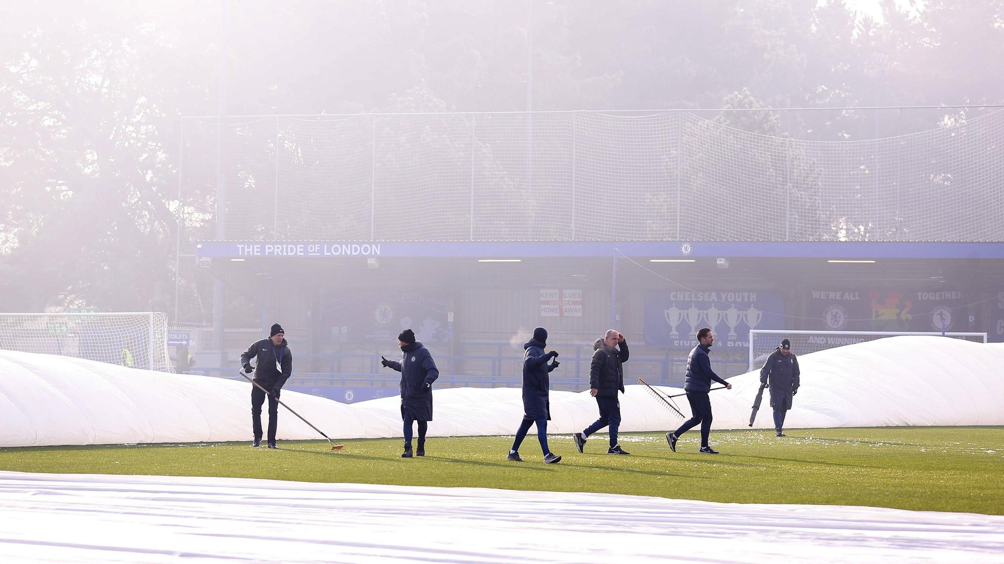 Zahlreiche Helfer versuchen vergeblich, den teils abgedeckten Platz im Stadion der Frauen des FC Chelsea bespielbar zu machen.
