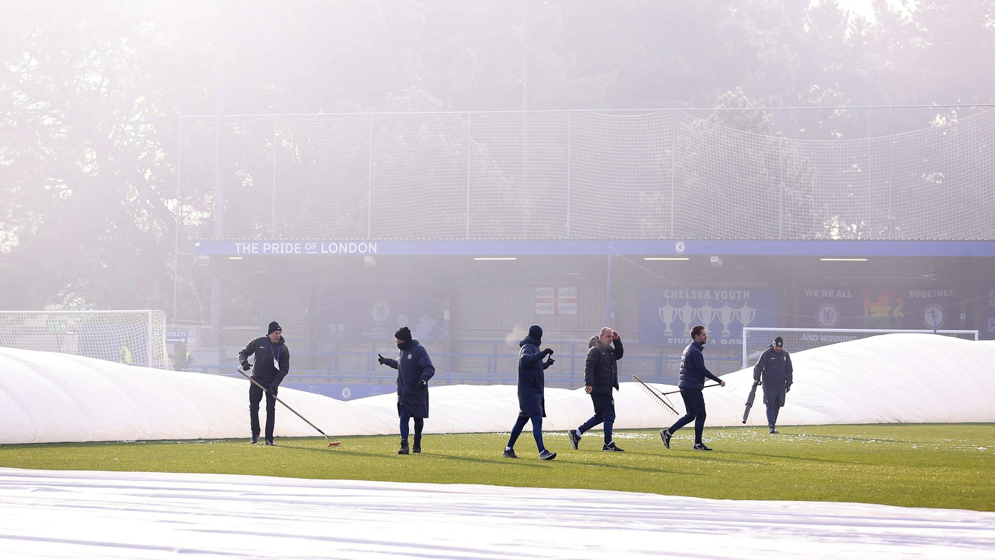 Zahlreiche Helfer versuchen vergeblich, den teils abgedeckten Platz im Stadion der Frauen des FC Chelsea bespielbar zu machen.