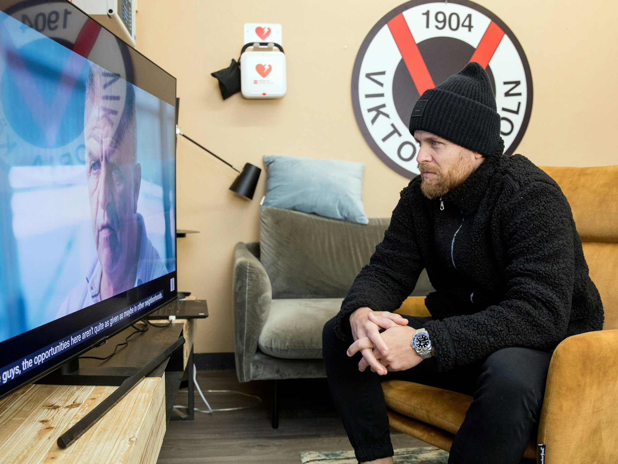 Fußballspieler Mike Wunderlich (Viktoria Köln) sitzt auf dem Sessel und schaut TV.