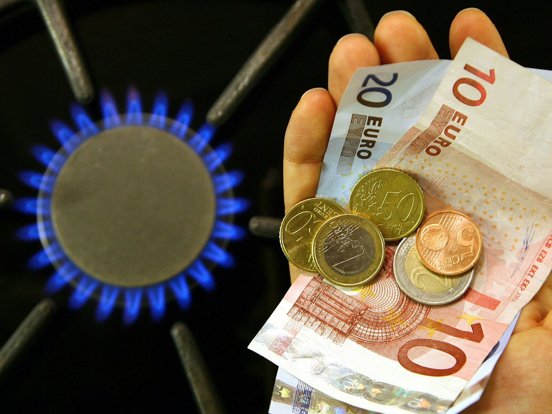 Neben einer brennenden Gasflamme an einem Herd in einer Küche im brandenburgischen Petersdorf (Oder-Spree) hält eine Frau im Oktober 2006 Geld in der Hand. Sinkende Großhandelspreise für Gas sorgen bei Verbraucherschützern für große Erwartungen.