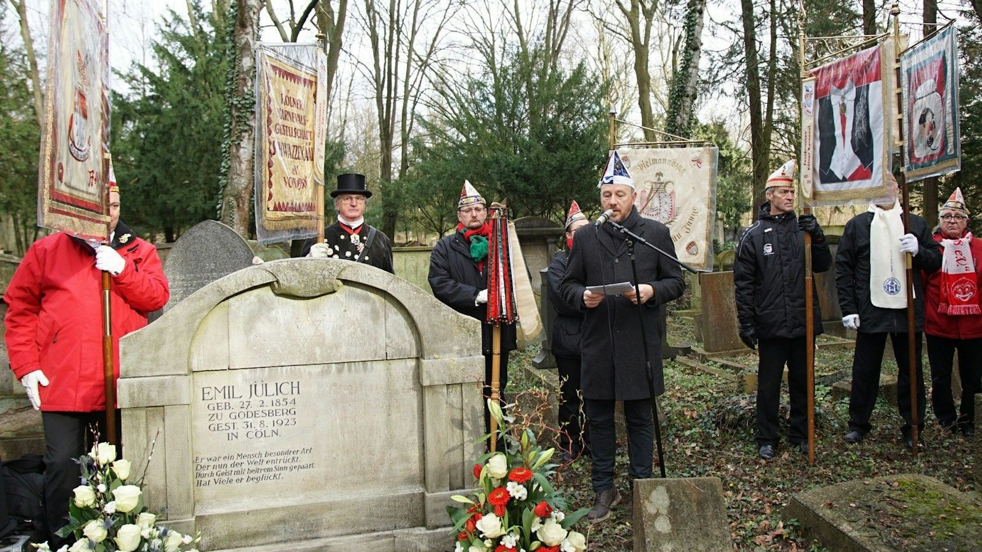 Karnevalisten und Karnevalistinnen stehen am Grab.