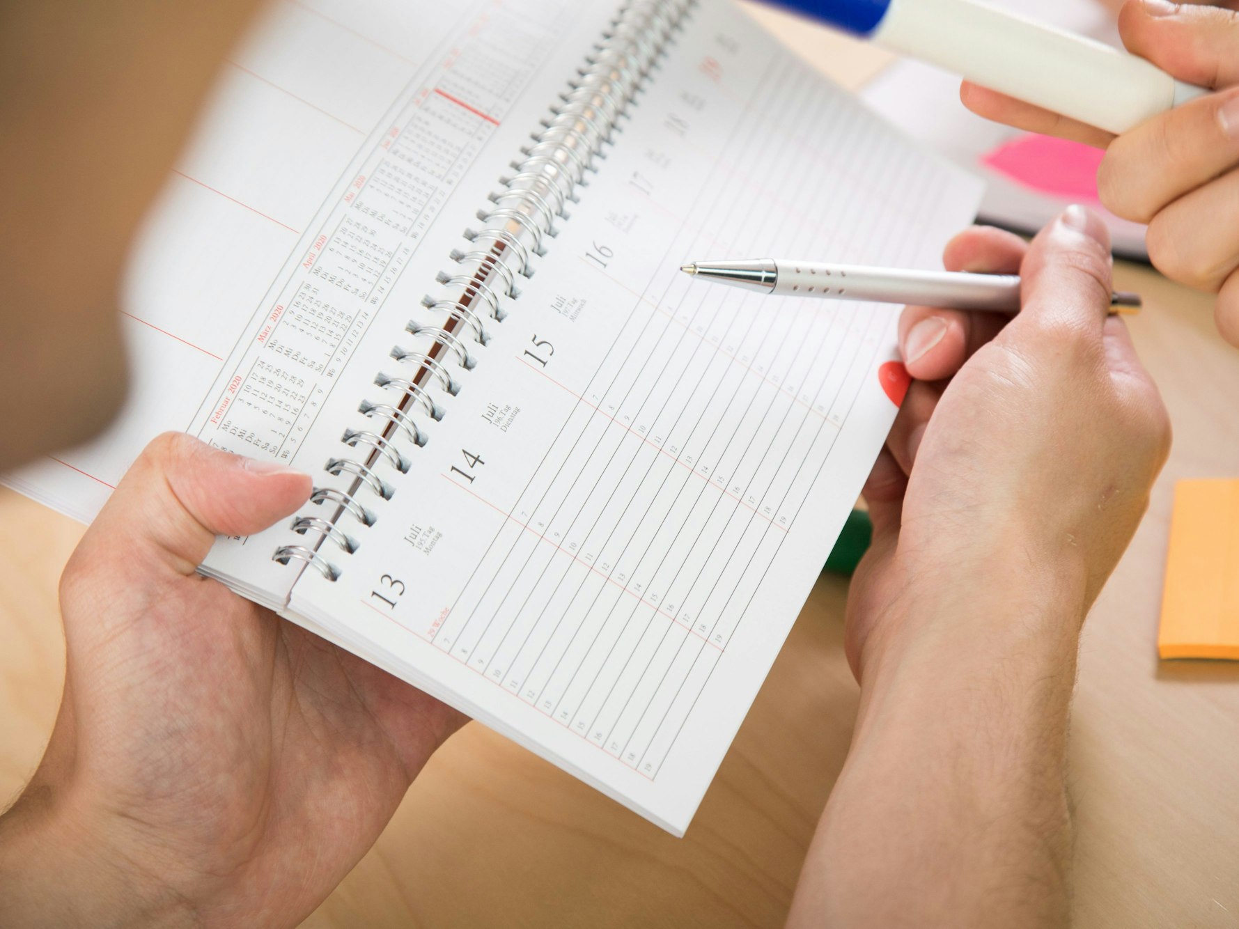Eine Person, hier im Juni 2020, hält einen Kalender und einen Stift in der Hand, um Urlaub zu planen. Resturlaub verfällt ohne Vorwarnung des Arbeitgebers nicht mehr. Was Arbeitnehmer und Arbeitnehmerinnen beim Urlaubsantrag nun beachten sollten.