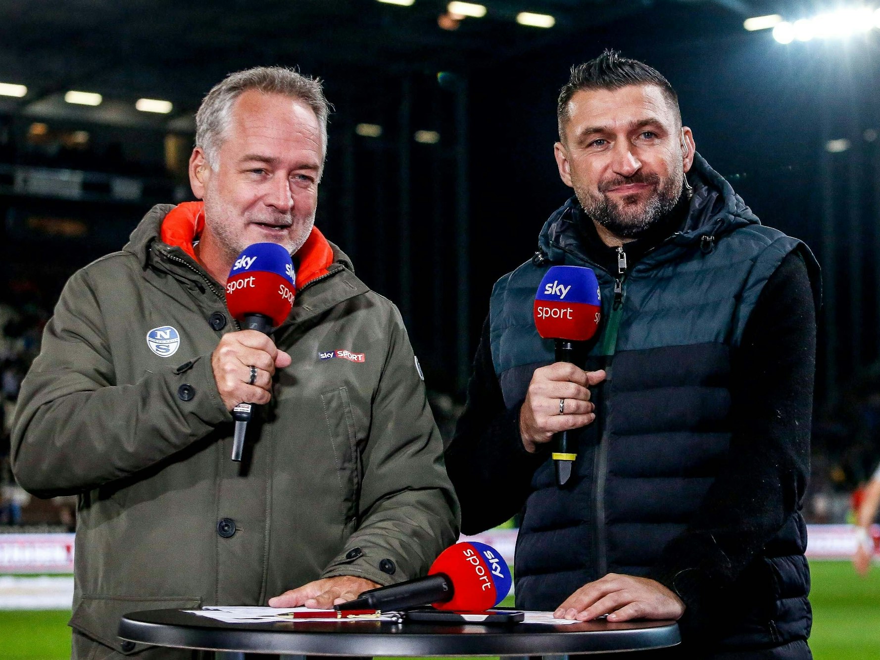 Sky-Moderator Stefan Hempel und Experte Torsten Mattuschka stehen am Tisch.