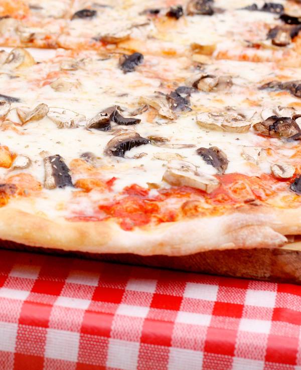 Eine Pizza Funghi (mit Pilzen) liegt auf einem Tisch.
