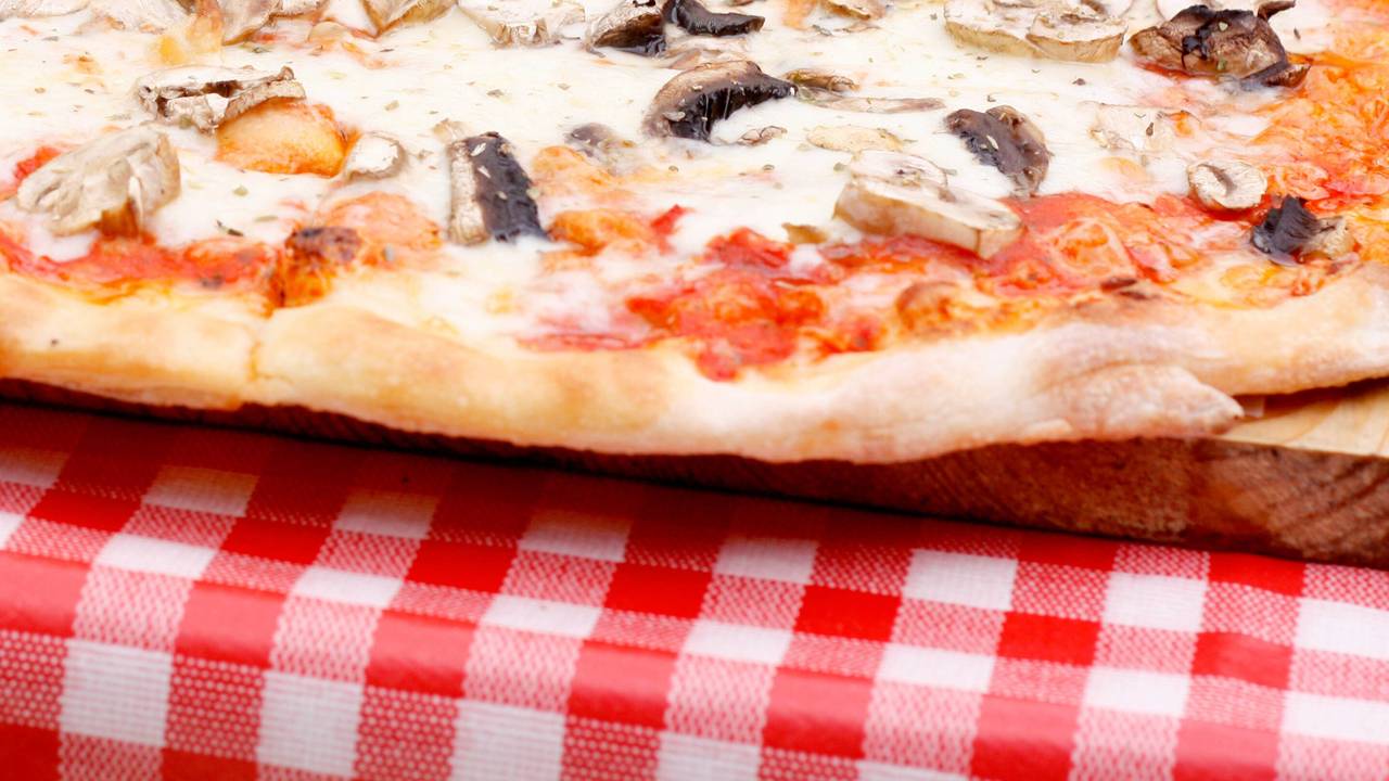 Eine Pizza Funghi (mit Pilzen) liegt auf einem Tisch.