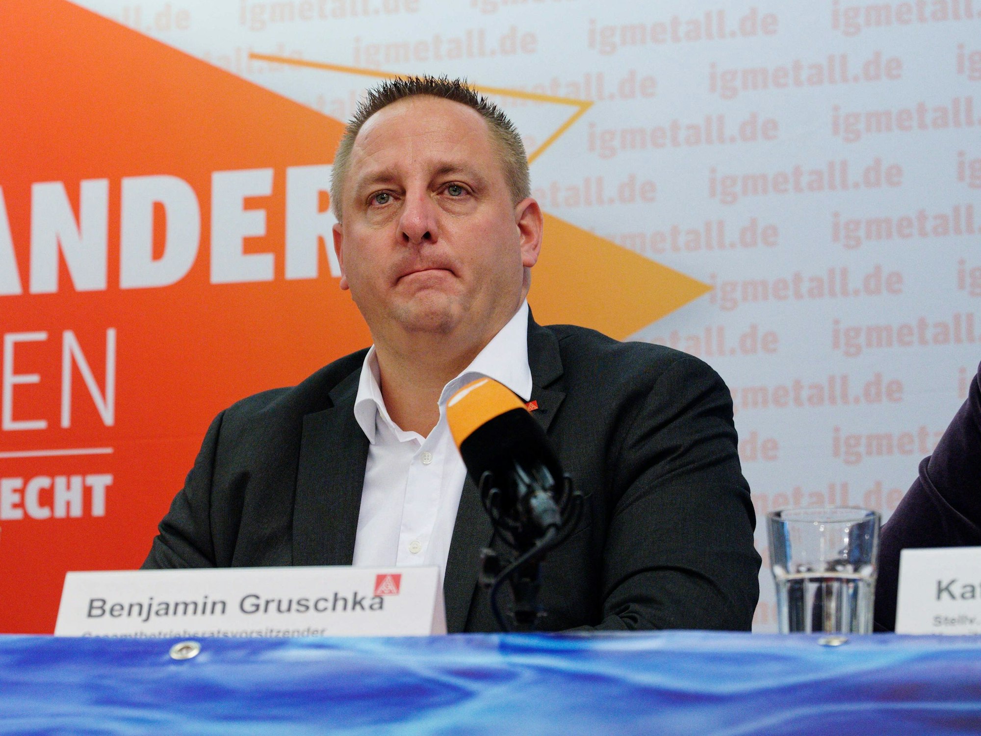 Benjamin Gruschka sitzt auf einer Bühne vor Mikrofonen und beantwortet Fragen.