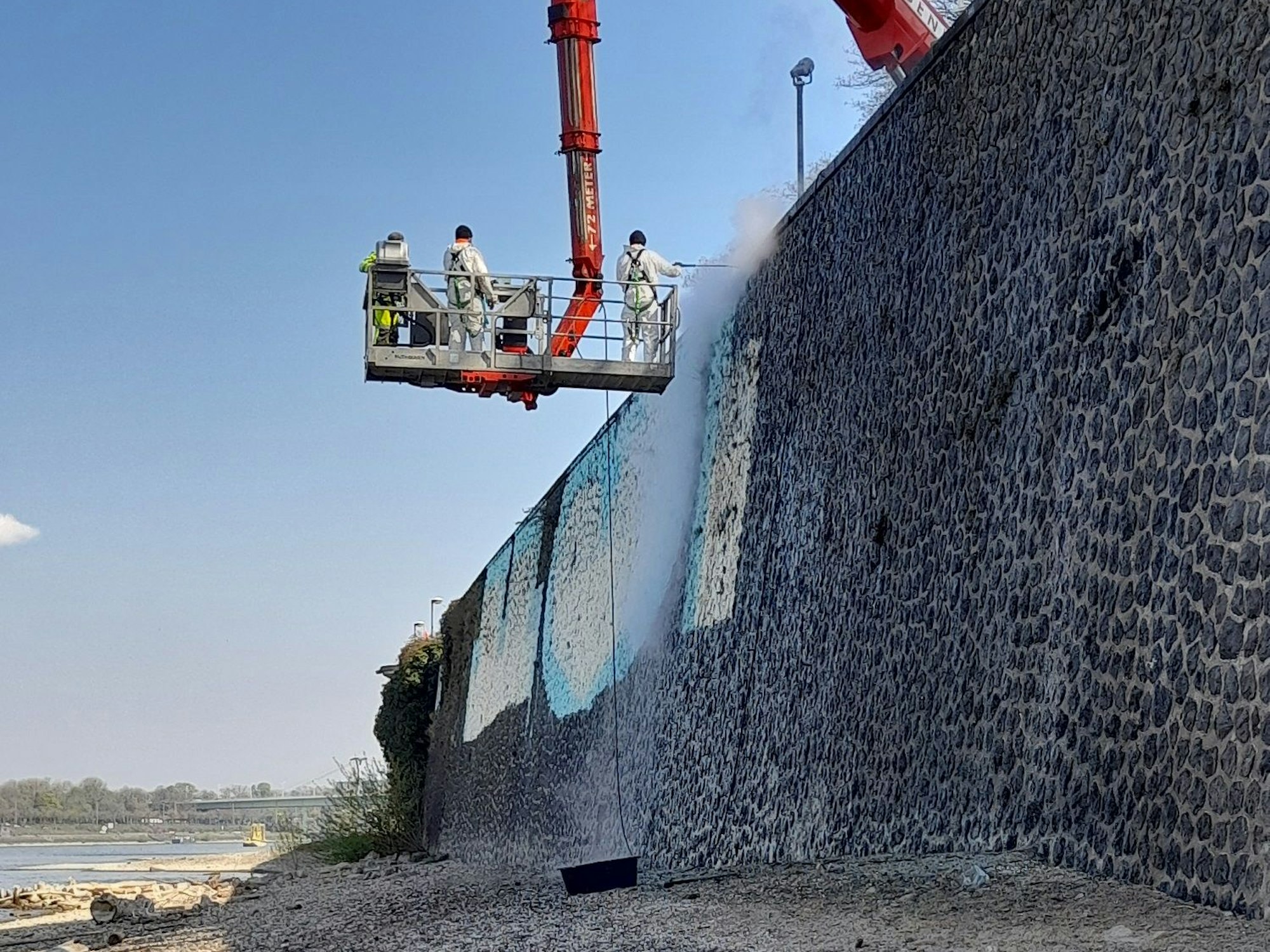 Arbeiter der AWB entfernen mit einer Hebebühne ein großes Graffito in Köln.