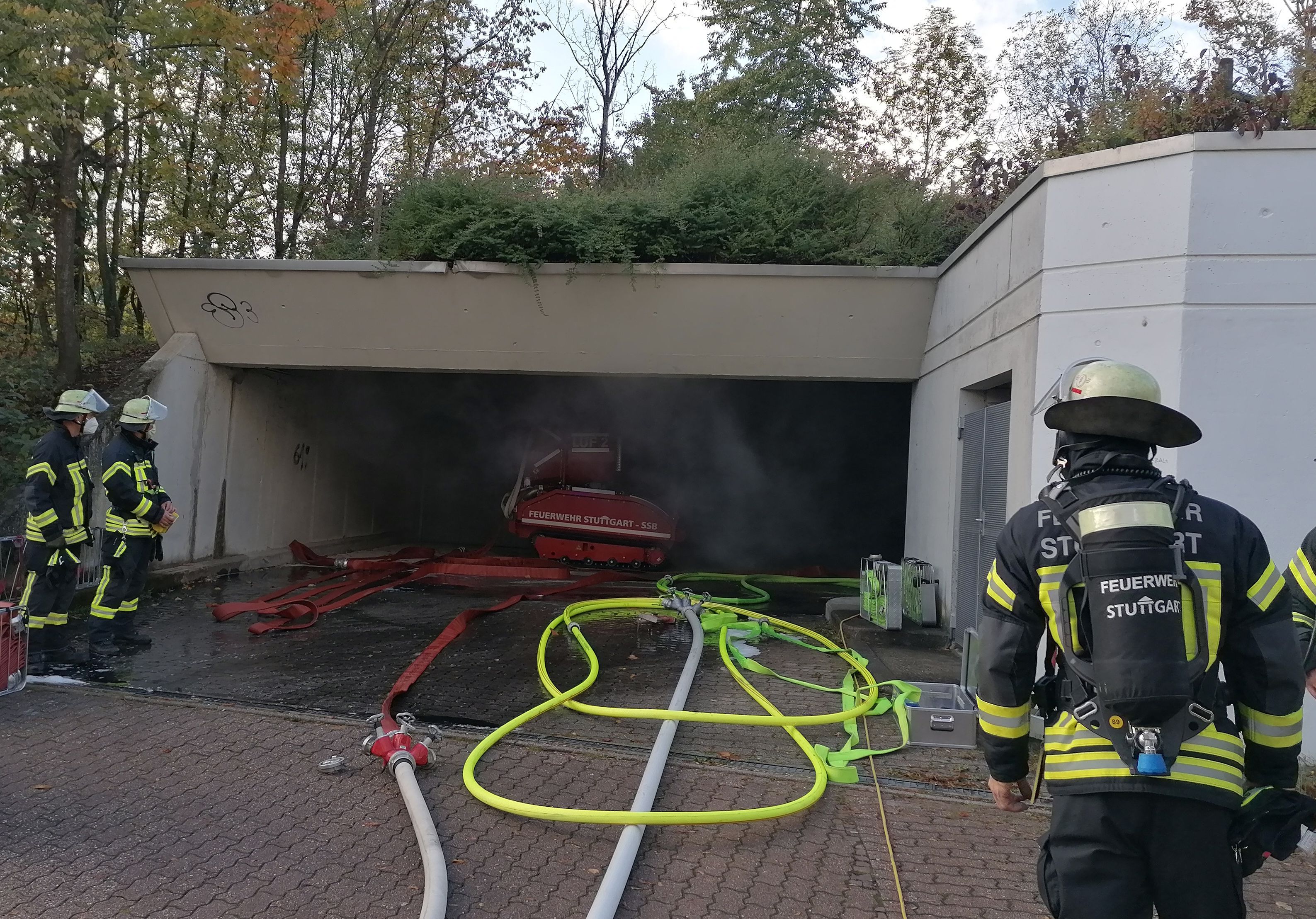 Feuerwehrleute stehen an der Zufahrt einer Tiefgarage, aus der Rauch quillt.