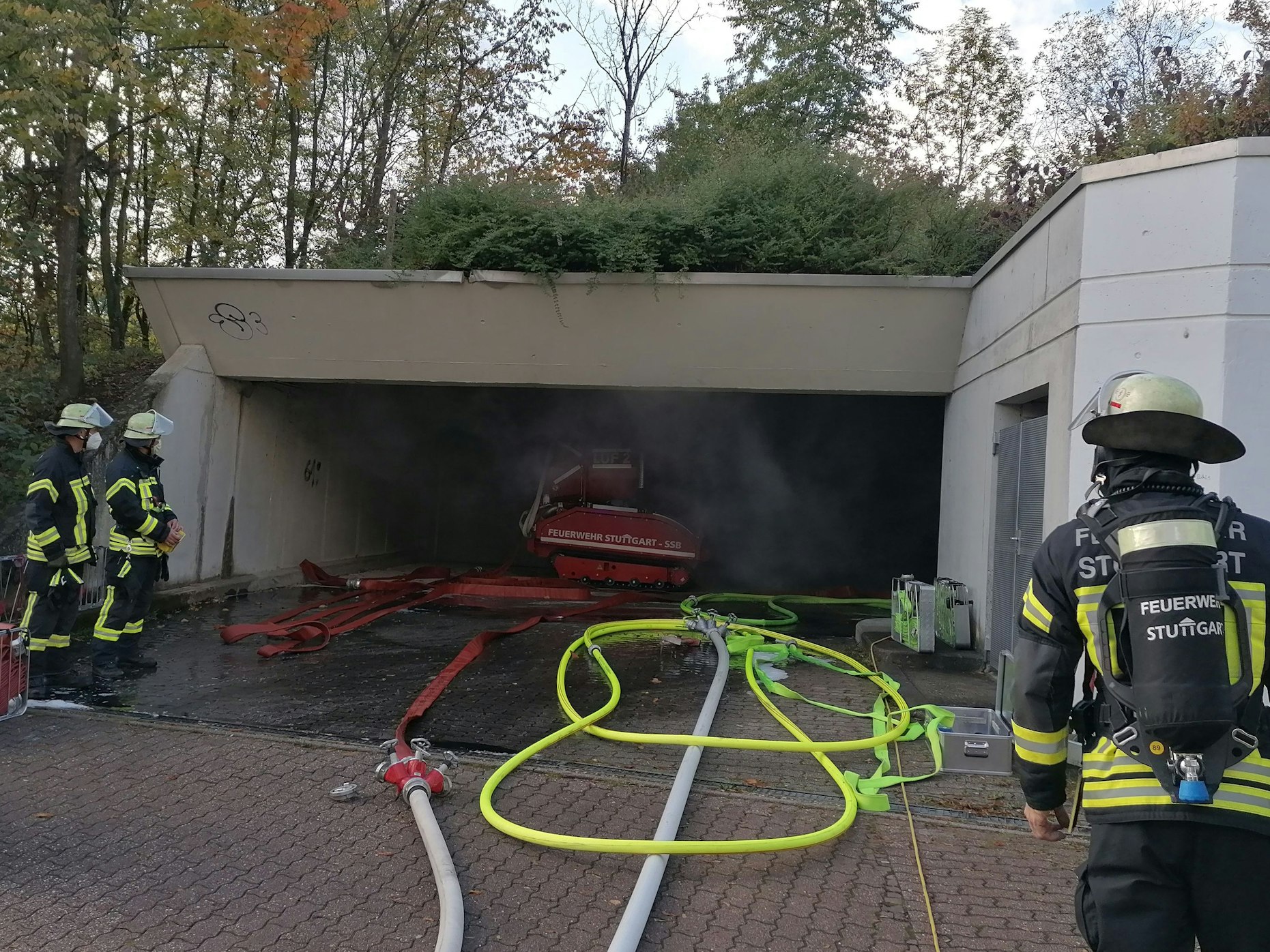 Feuerwehrleute stehen an der Zufahrt einer Tiefgarage, aus der Rauch quillt.