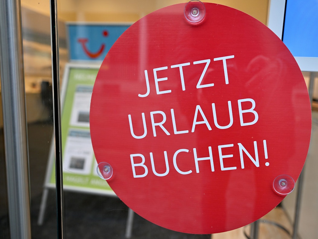 Das undatierte Symbolfoto zeigt ein Schaufenster mit einem runden roten Aufkleber und den Worten „Jetzt Urlaub buchen!“.