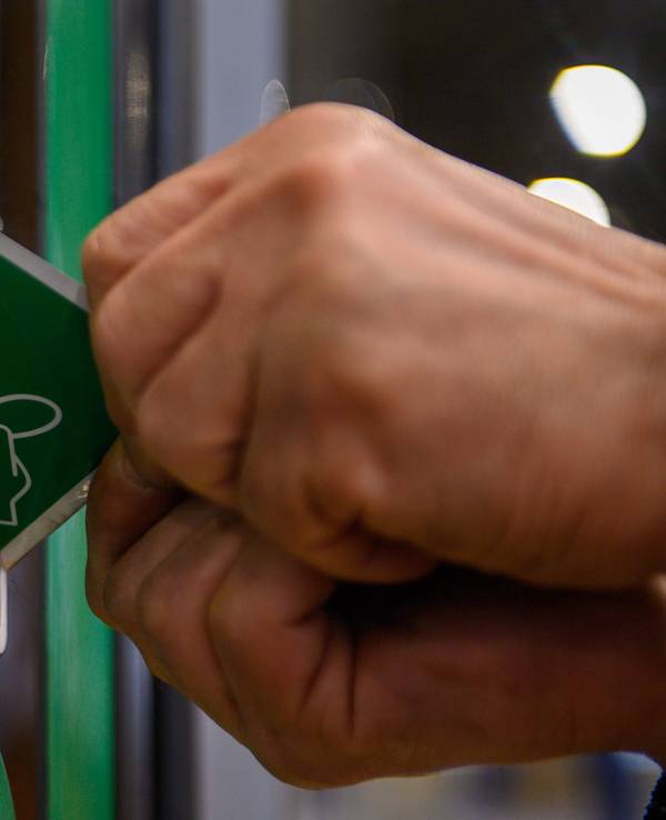Das Foto von Dezember 2022 zeigt einen grünen Aufkleber, der auf die Maskenpflicht im ÖPNV hinweist, und von einer Scheibe abgezogen wird.