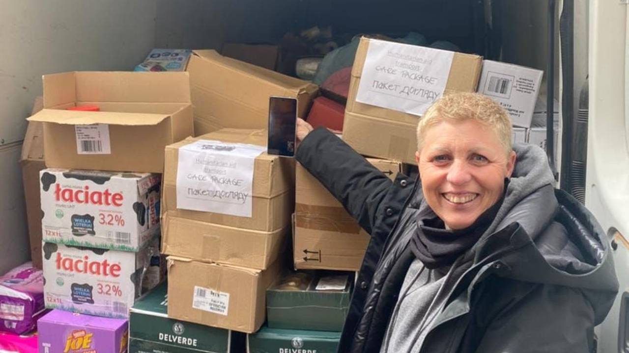 Eine Frau steht neben einem mit Kisten beladenen Transporter.