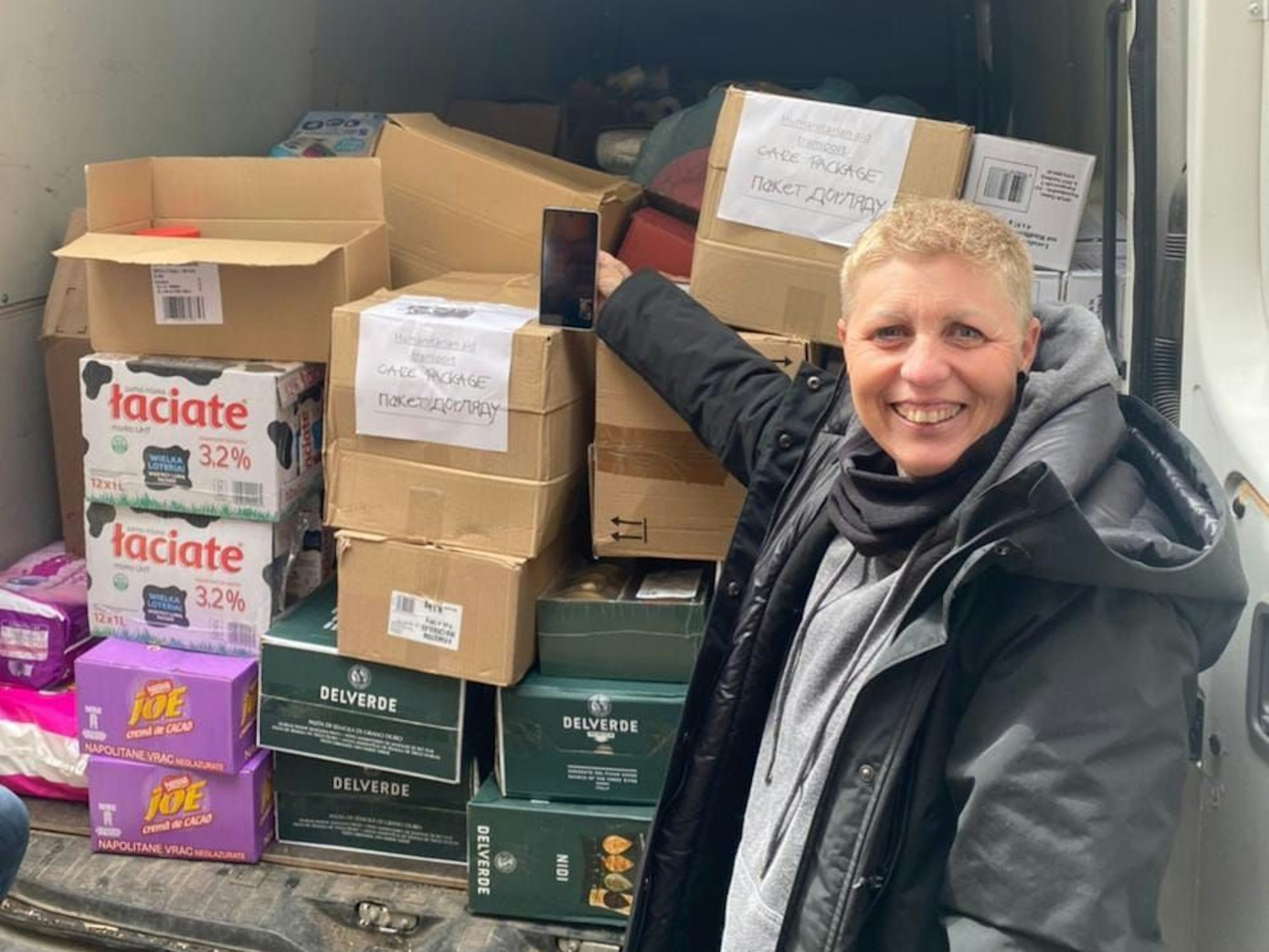 Eine Frau steht neben einem mit Kisten beladenen Transporter.