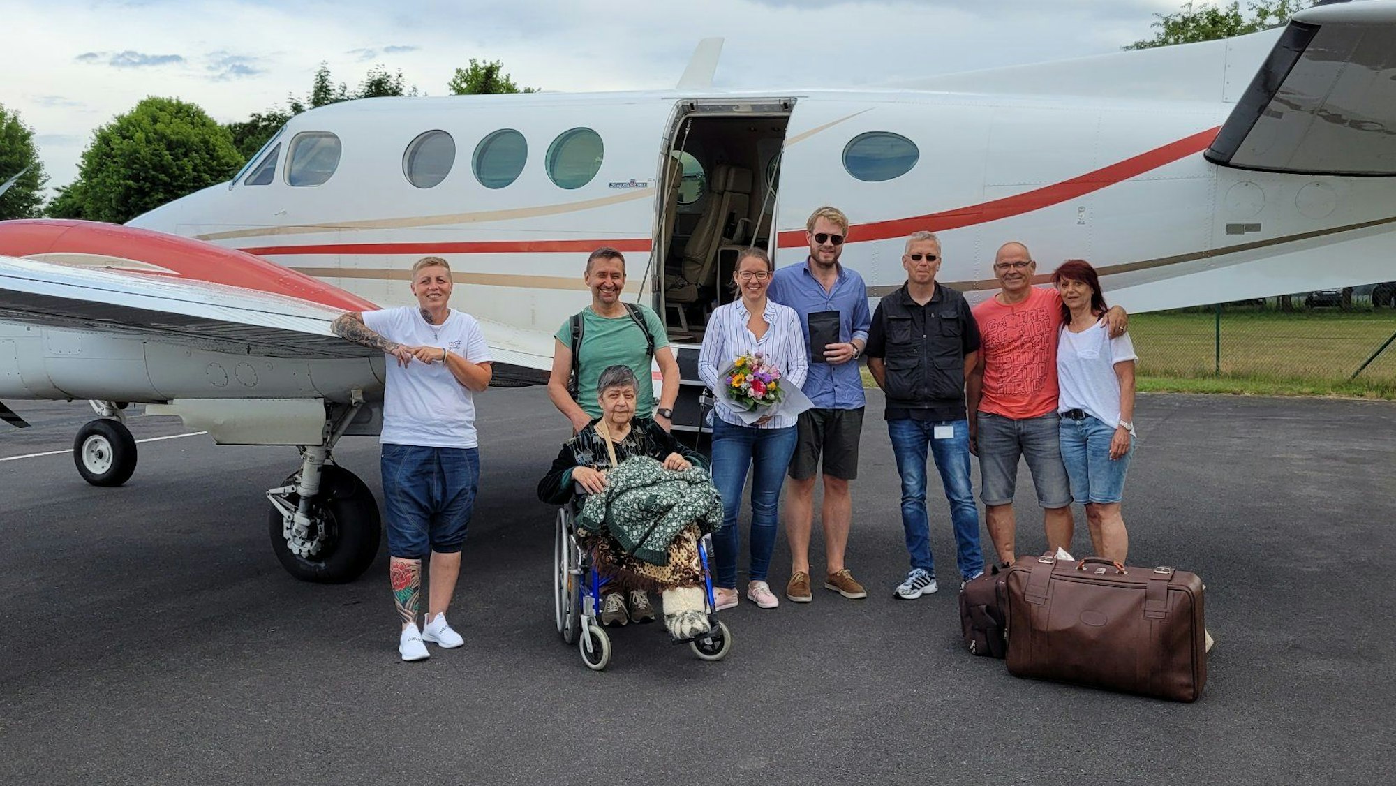 Eine Gruppe steht auf einem Flugplatz vor einem Flugzeug.