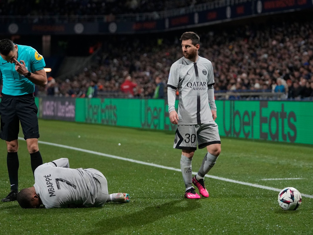 Kylian Mbappé krümmt sich im Spiel von Paris Saint-Germain bei HSC Montpellier am Boden. Lionel Messi und der Schiedsrichter stehen neben ihm.