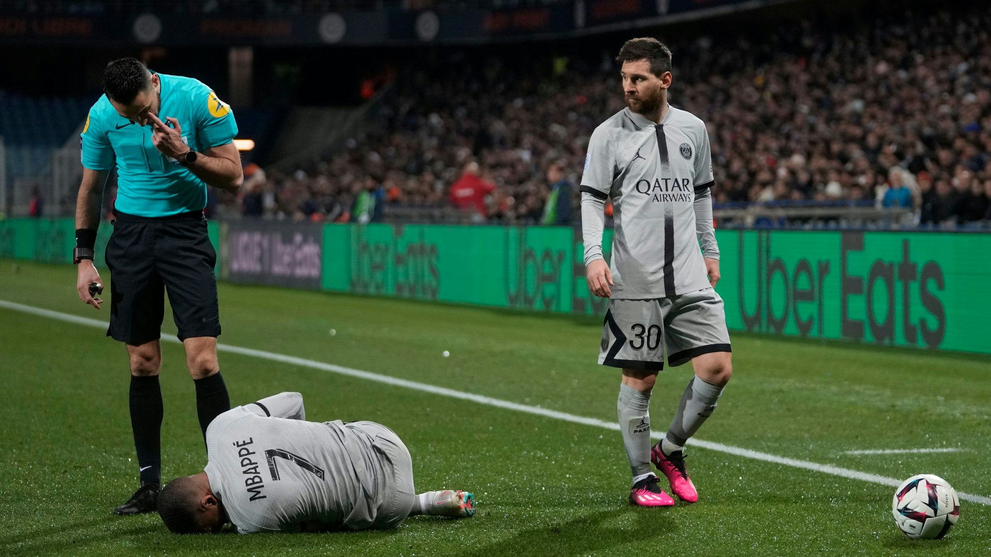 Kylian Mbappé krümmt sich im Spiel von Paris Saint-Germain bei HSC Montpellier am Boden. Lionel Messi und der Schiedsrichter stehen neben ihm.