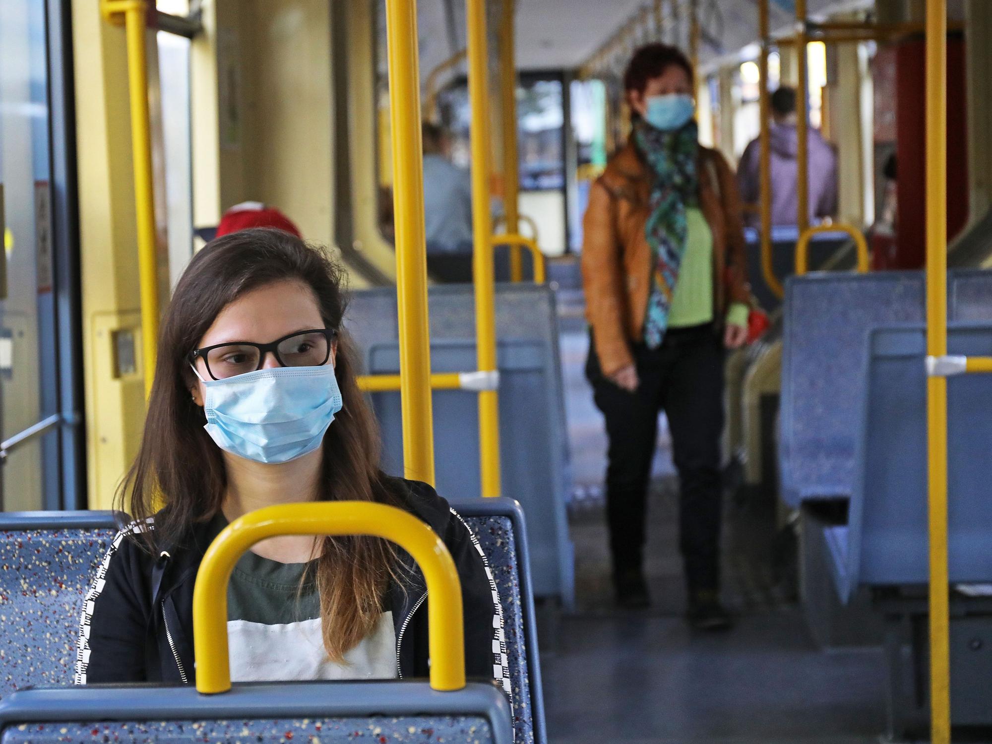 Eine Frau sitzt mit einer Schutzmaske in einer Straßenbahn.