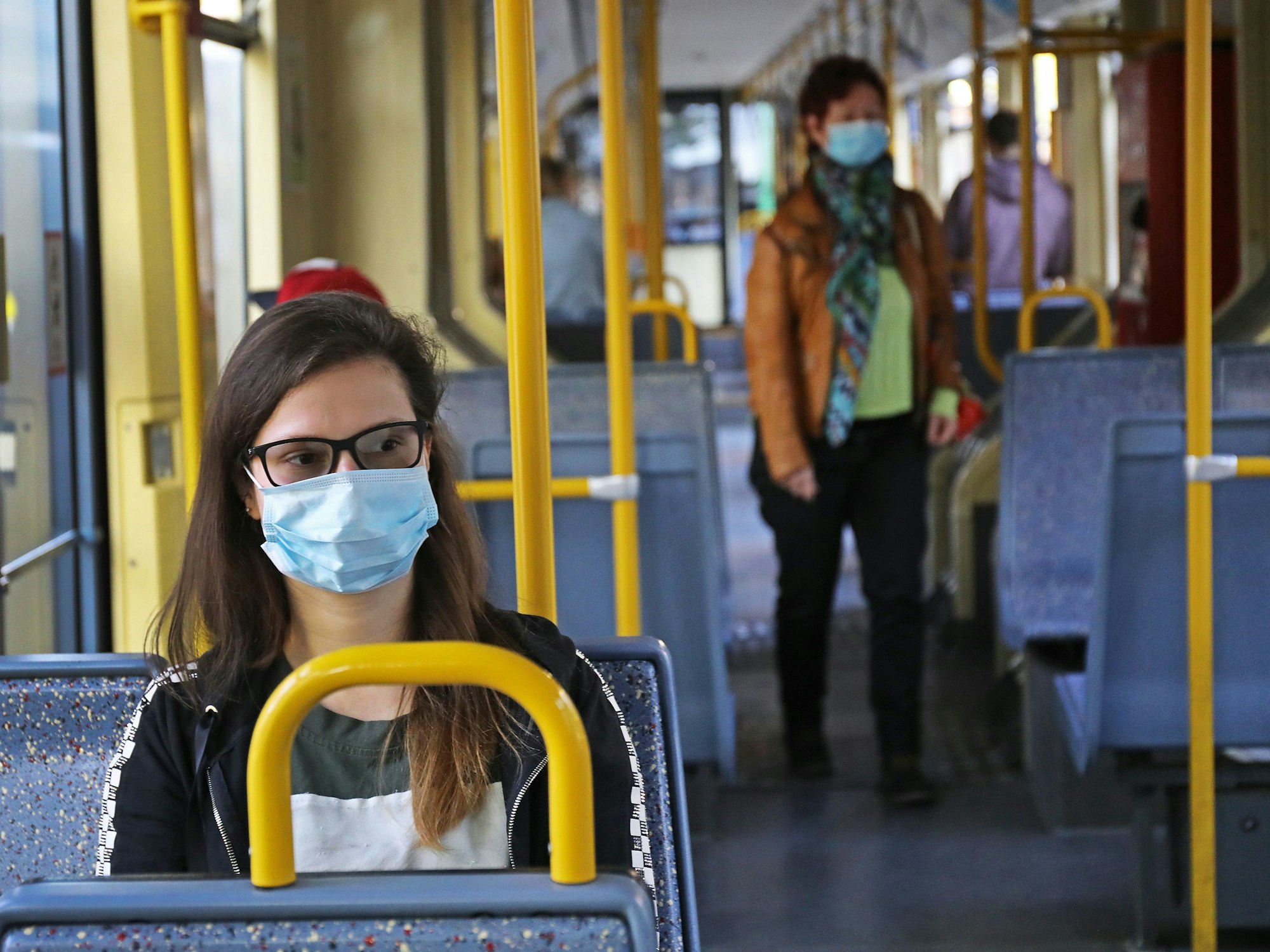 Eine Frau sitzt mit einer Schutzmaske in einer Straßenbahn.